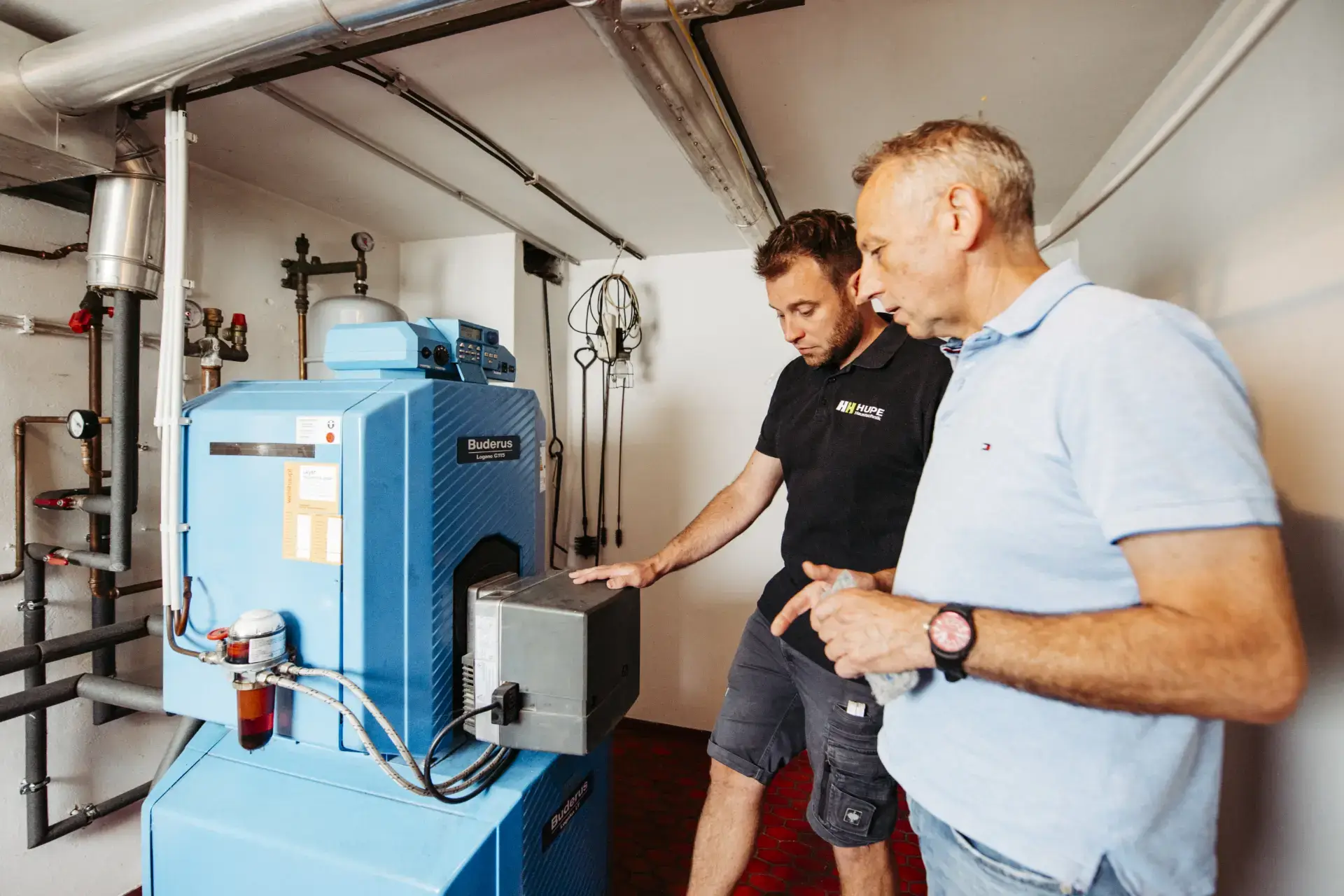 Mitarbeiter von Hupe Haustechnik bespricht mit einem Kunden den alten Ölkessel im Heizungskeller