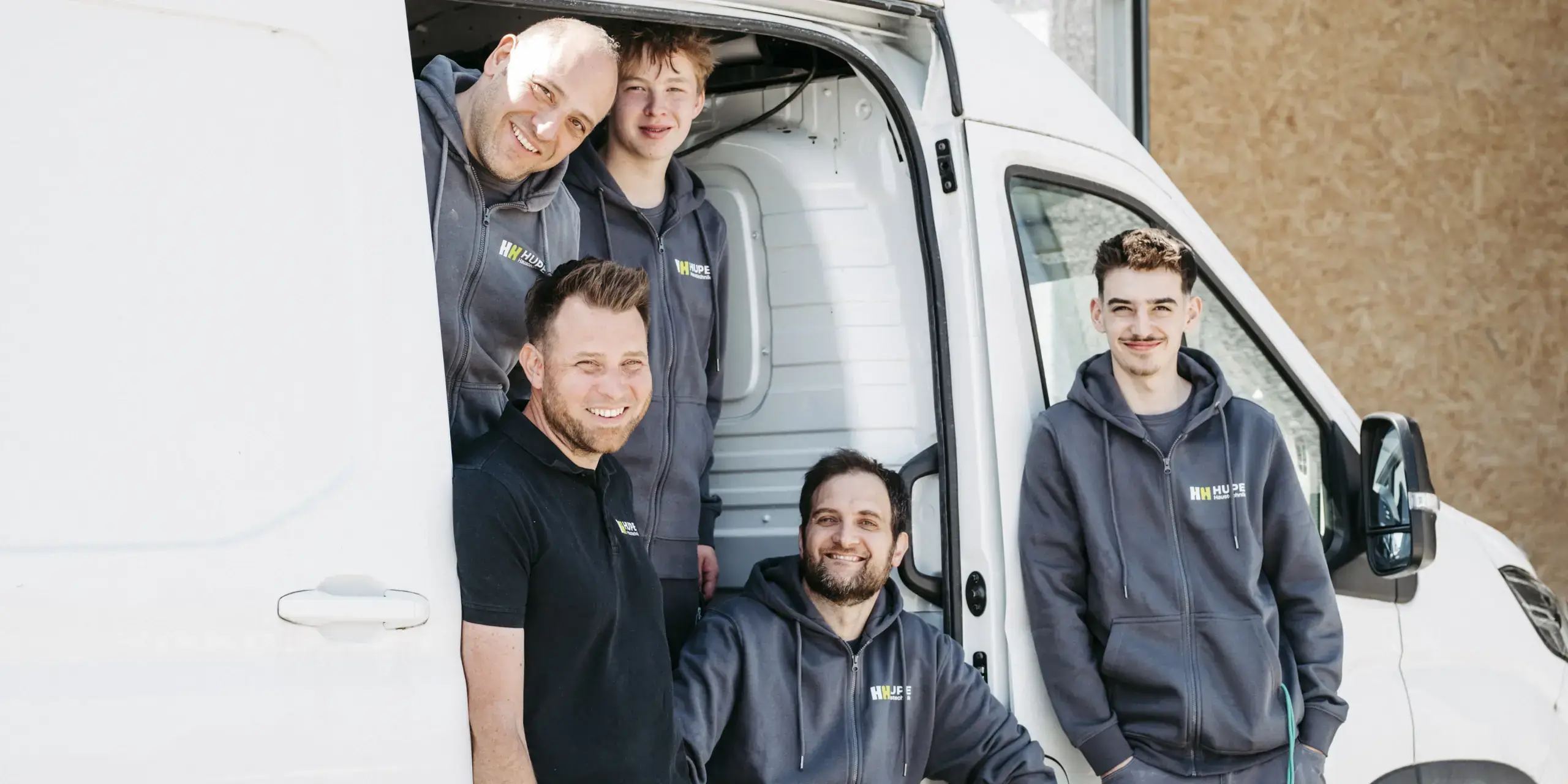 Fünf Mitarbeiter von Hupe Haustechnik in Firmenkleidung an der offenen Schiebetür eines Transporters